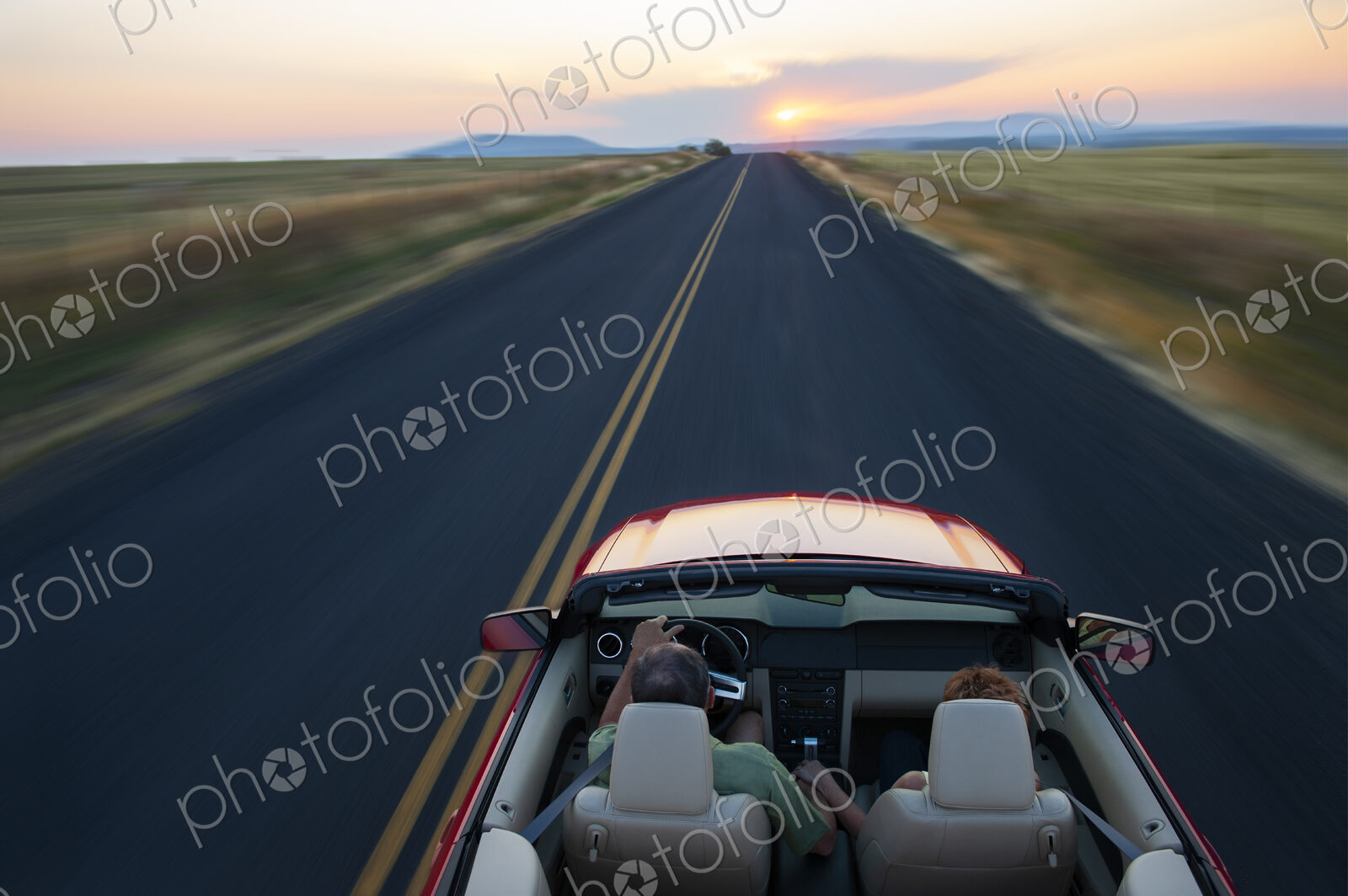 View from behind of senior couple in a convertible sports car driving on a highway at…
