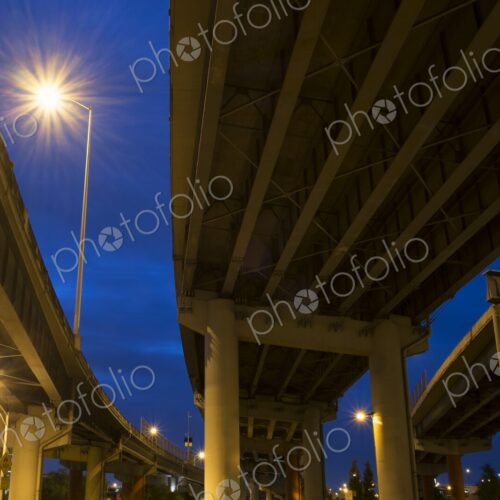 View from below of I-5 freeway overpass at night in Portland, Oregon. Streetlights…
