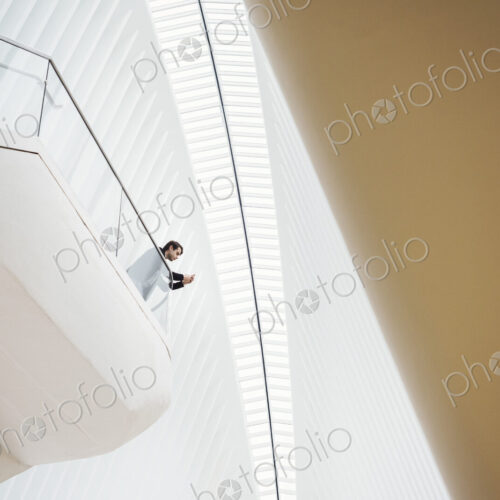 View from below of a man standing on a balcony in the Oculus building looking at his…