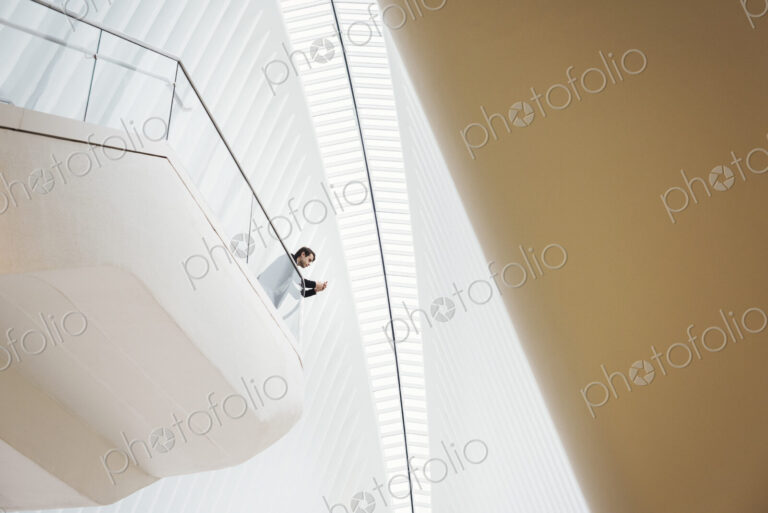 View from below of a man standing on a balcony in the Oculus building looking at his…