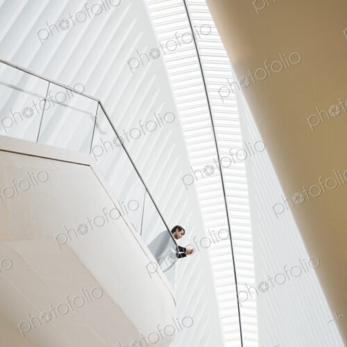 View from below of a man standing on a balcony in the Oculus building on his phone,… View from below of a man standing on a balcony in the Oculus building on his phone,…