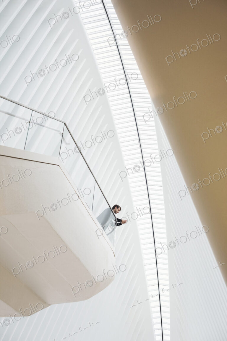 View from below of a man standing on a balcony in the Oculus building on his phone,…
