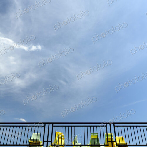View from below of yellow and blue chairs on a terrace. View from below of yellow and blue chairs on a terrace.