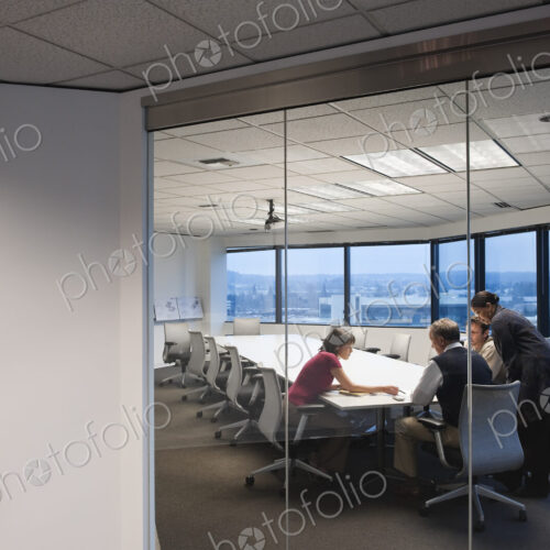 View from outside a conference room looking in at a team of people working late in the…