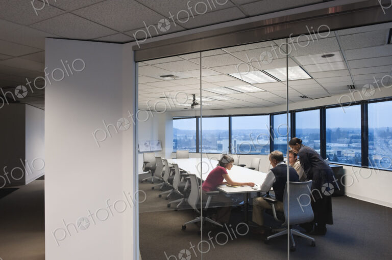 View from outside a conference room looking in at a team of people working late in the…