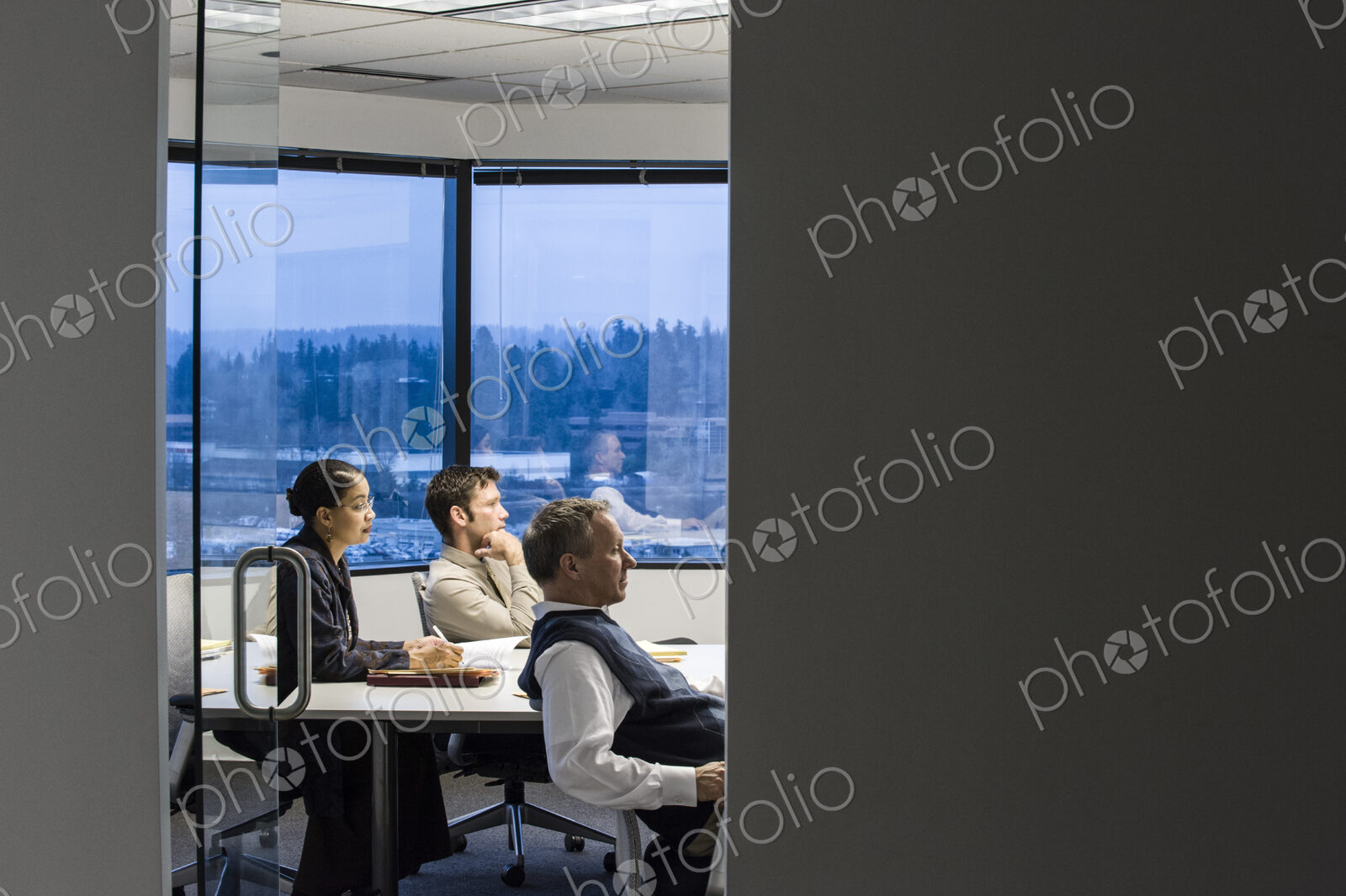 View from outside of a conference room looking in at a mixed race group of business…