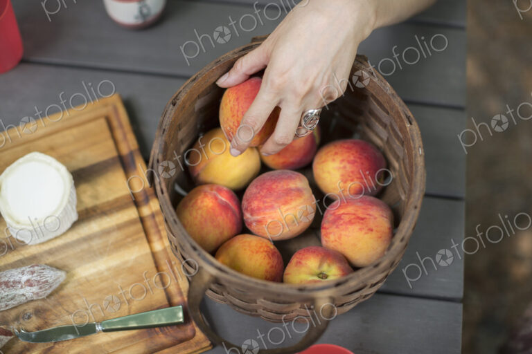 View from overhead of a picnic table with a basket of fresh peaches and a cheese board.
