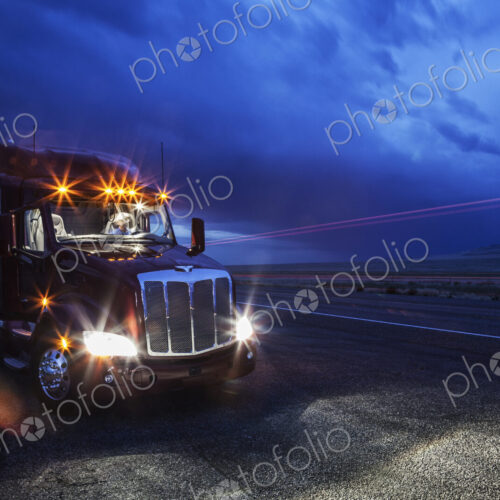 View into the cab of a commercial truck with a driver in the front seat at night.