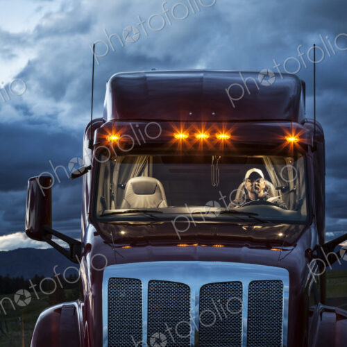 View into the cab of a commercial truck with a driver in the front seat at night. View into the cab of a commercial truck with a driver in the front seat at night.