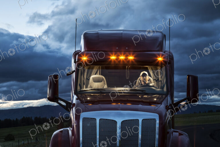 View into the cab of a commercial truck with a driver in the front seat at night.