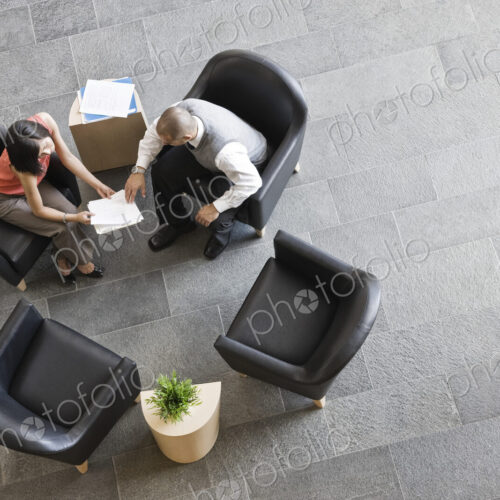 View looking down on a businessman and businesswoman sitting and talking in office…