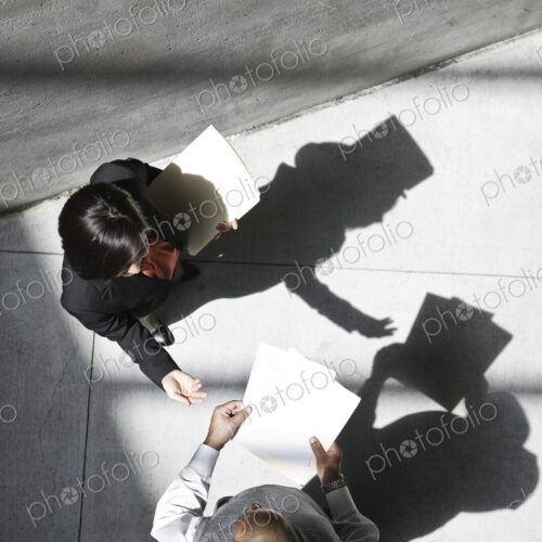 View looking down on a businesswoman and businessman talking in an office building lobby.