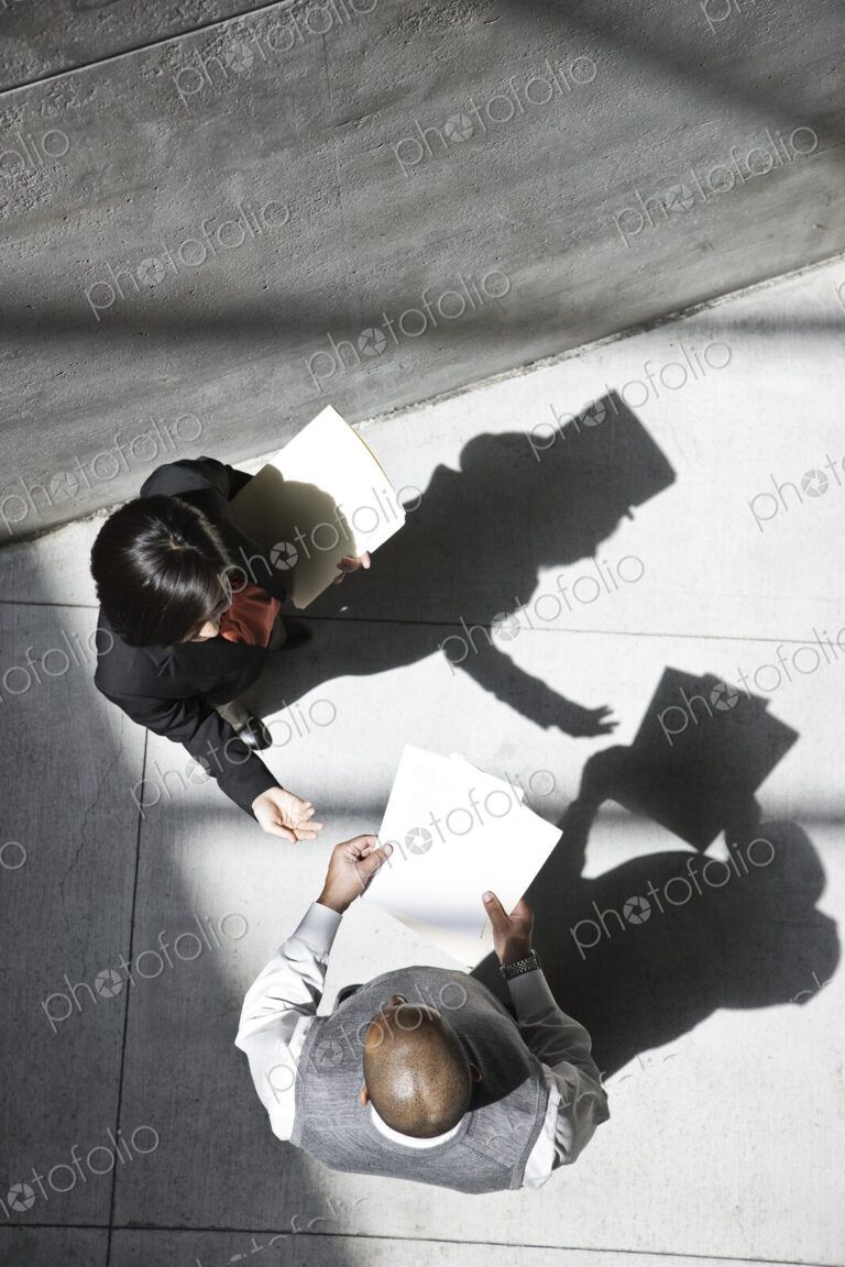 View looking down on a businesswoman and businessman talking in an office building lobby.