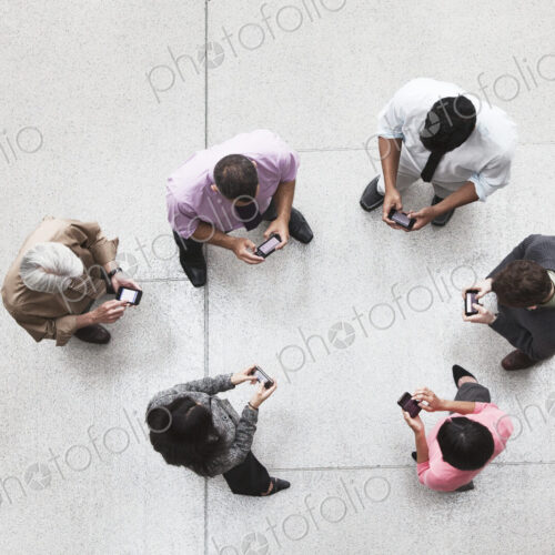 View looking down on a group of business people in a lobby area using their cell phones. View looking down on a group of business people in a lobby area using their cell phones.
