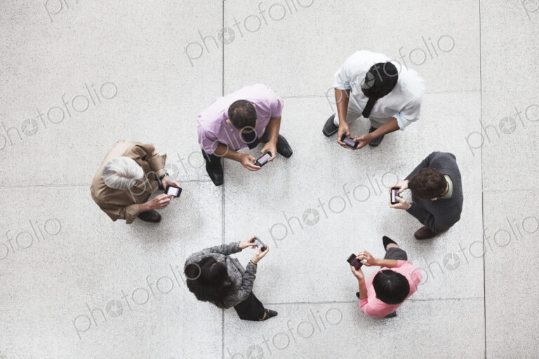 View looking down on a group of business people in a lobby area using their cell phones.