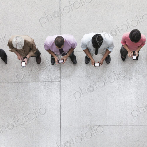View looking down on a group of business people in a lobby area using their cell phones. View looking down on a group of business people in a lobby area using their cell phones.