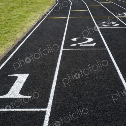 View of a black asphalt running track with white lane markings and numbers - a symbol…