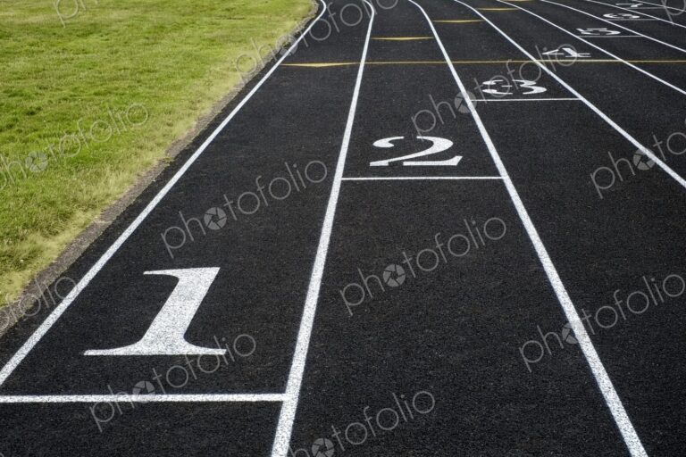 View of a black asphalt running track with white lane markings and numbers - a symbol…