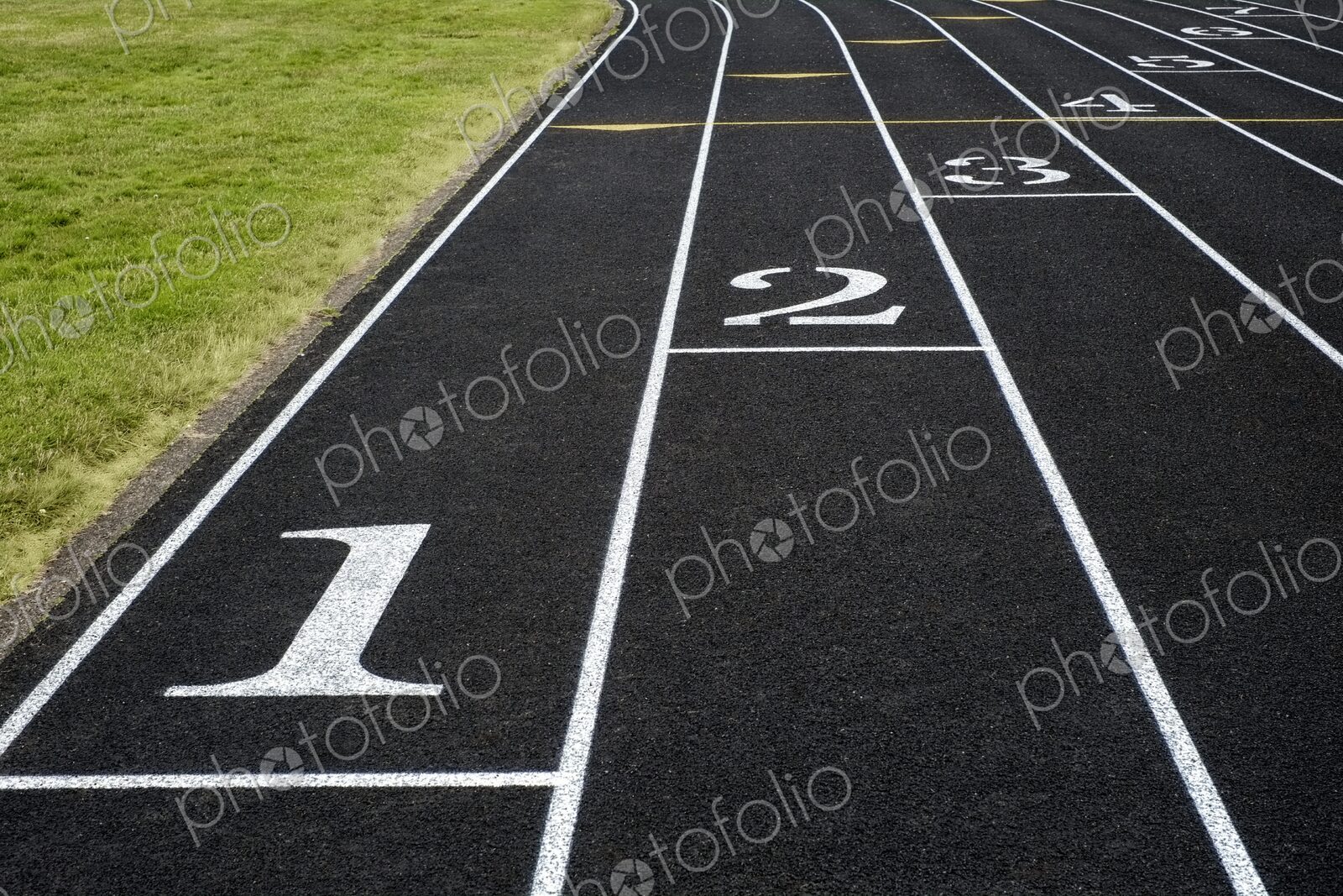 View of a black asphalt running track with white lane markings and numbers – a symbol…