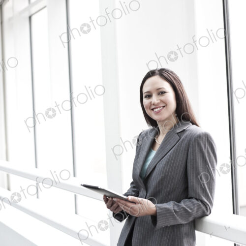 View of a caucasian business woman in a suit coat standing in a covered glass walkway.
