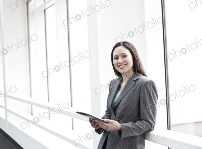View of a caucasian business woman in a suit coat standing in a covered glass walkway.