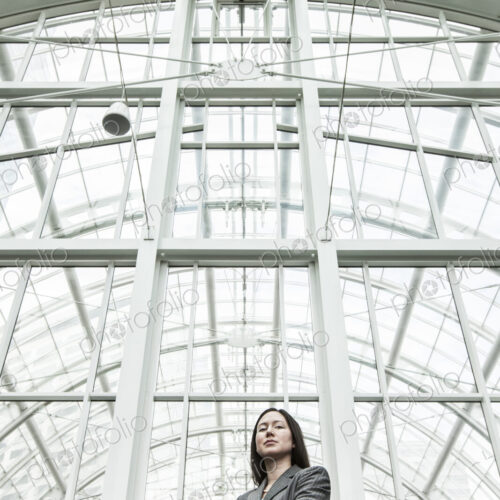 View of a caucasian business woman in a suit coat standing in a covered glass walkway. View of a caucasian business woman in a suit coat standing in a covered glass walkway.