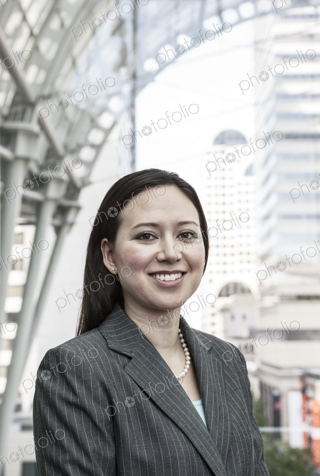 View of a caucasian business woman in a suit coat standing in a covered glass walkway.