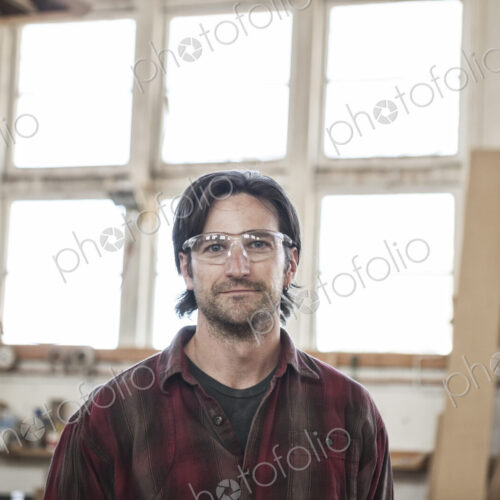 View of a caucasian man factory worker wearing safetly glasses in a woodworking factory.