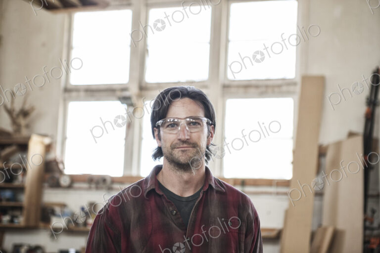 View of a caucasian man factory worker wearing safetly glasses in a woodworking factory.