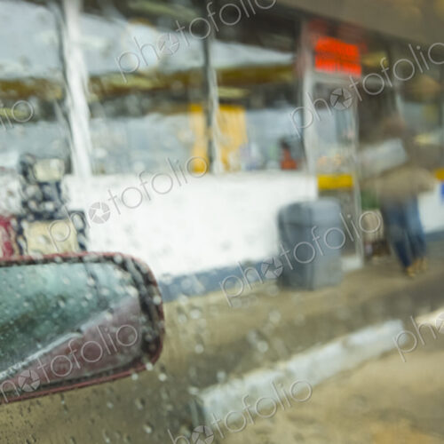 View of a convenience store through a car window from the parking lot in heavy rain,…