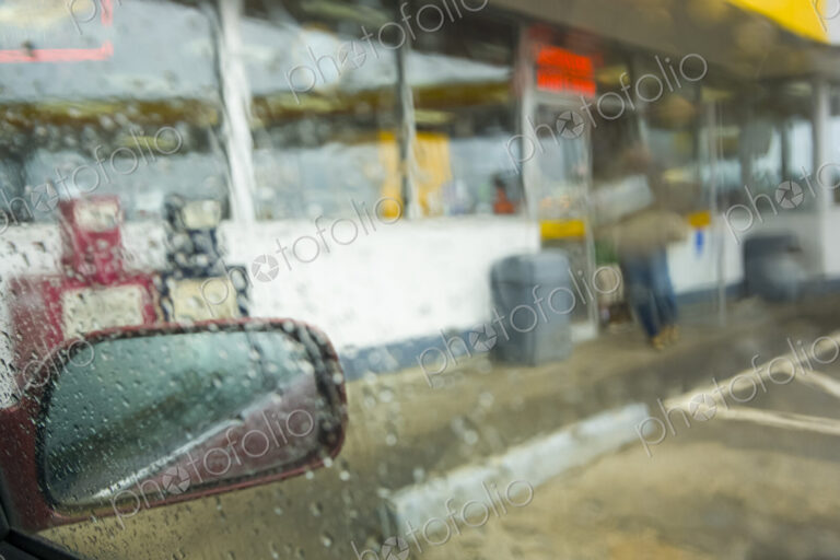 View of a convenience store through a car window from the parking lot in heavy rain,…