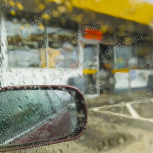 View of a convenience store through a car window from the parking lot in heavy rain,…