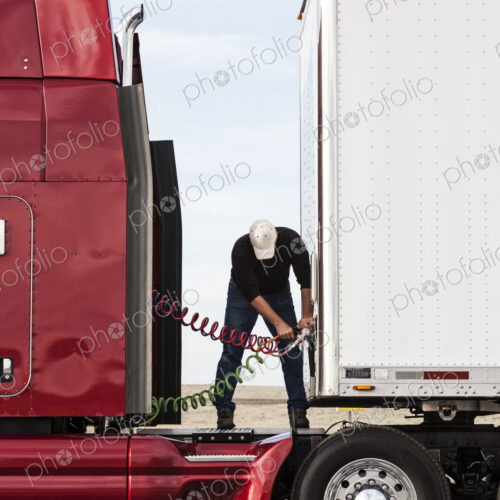 View of a driver connectiing the power cables to trailer of a commercial truck.