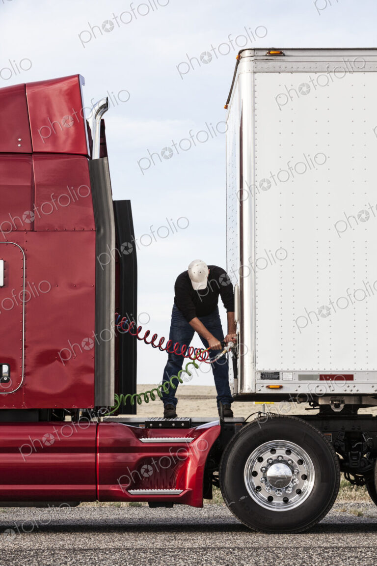 View of a driver connectiing the power cables to trailer of a commercial truck.