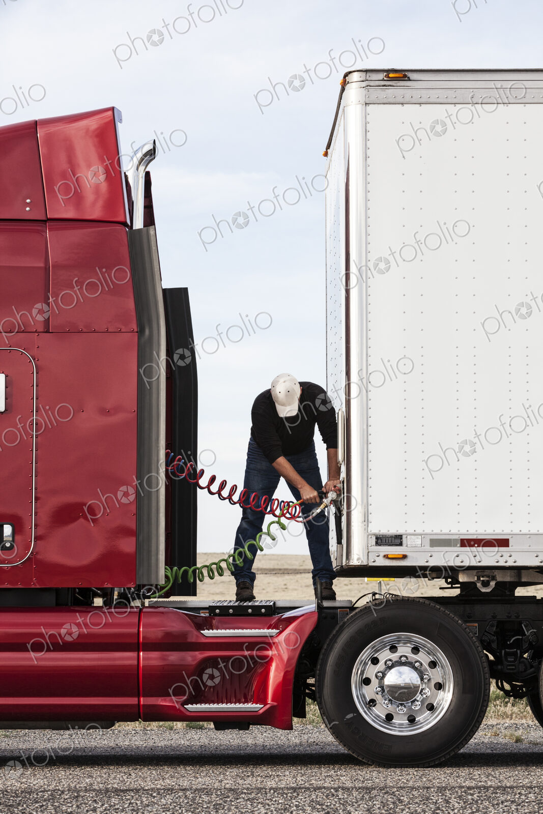View of a driver connectiing the power cables to trailer of a commercial truck.