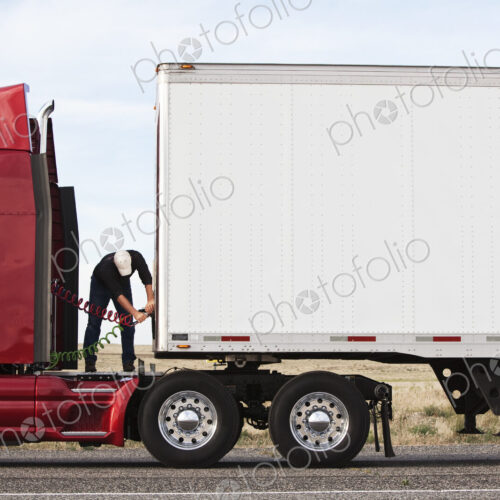 View of a driver connectiing the power cables to trailer of a commercial truck.