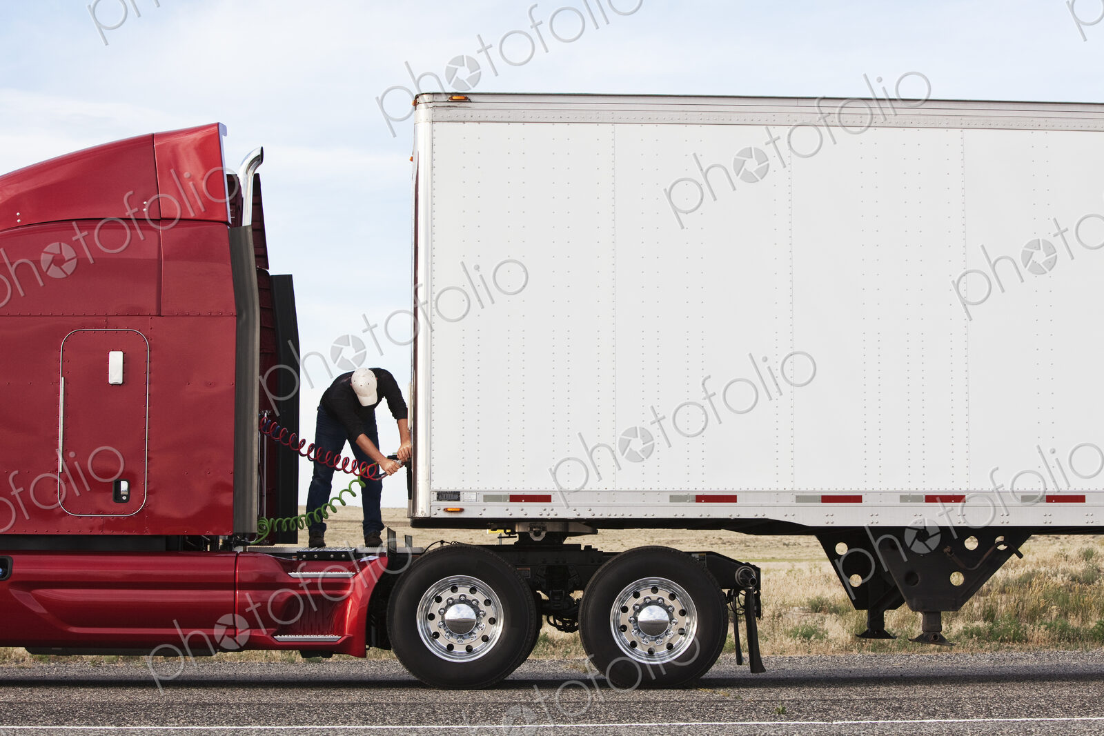 View of a driver connectiing the power cables to trailer of a commercial truck.