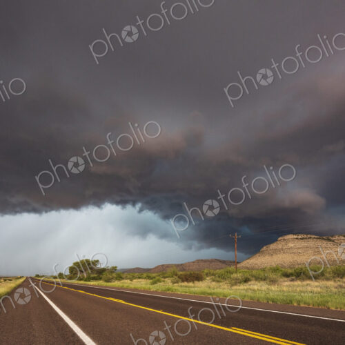 View of a road reaching the horizon, with black storm clouds above the road, the Texas… View of a road reaching the horizon, with black storm clouds above the road, the Texas…