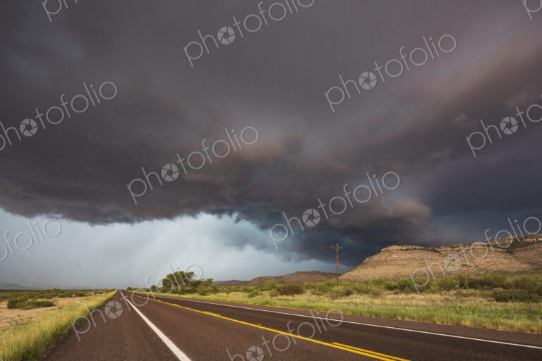 View of a road reaching the horizon, with black storm clouds above the road, the Texas…