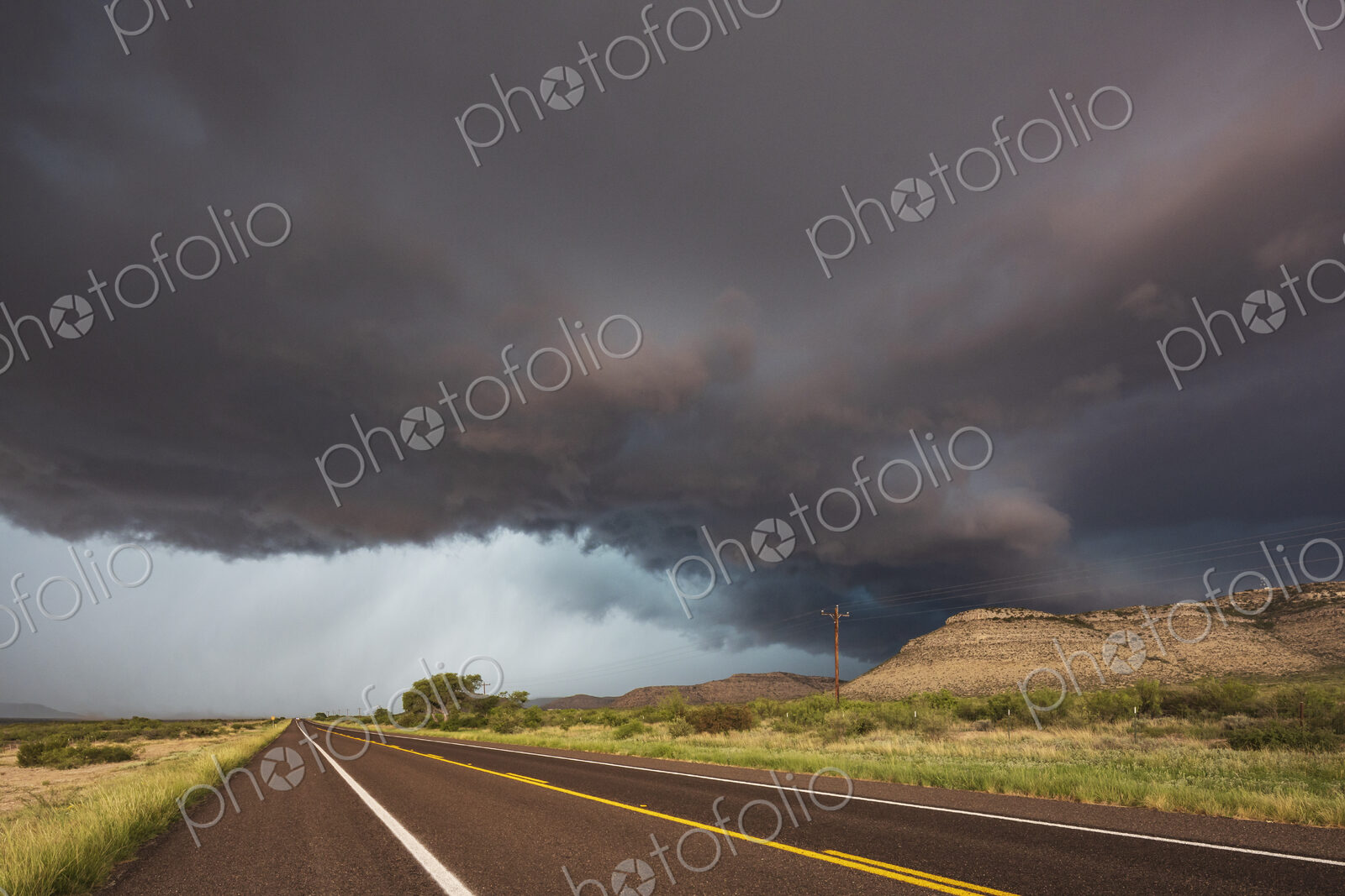 View of a road reaching the horizon, with black storm clouds above the road, the Texas…