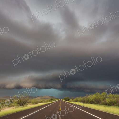 View of a road reaching the horizon, with black storm clouds above the road, the Texas… View of a road reaching the horizon, with black storm clouds above the road, the Texas…