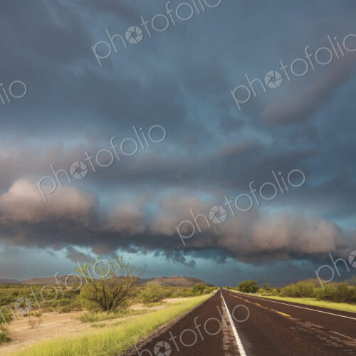 View of a road reaching the horizon, with black storm clouds above the road, the Texas… View of a road reaching the horizon, with black storm clouds above the road, the Texas…