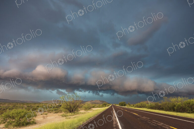 View of a road reaching the horizon, with black storm clouds above the road, the Texas…
