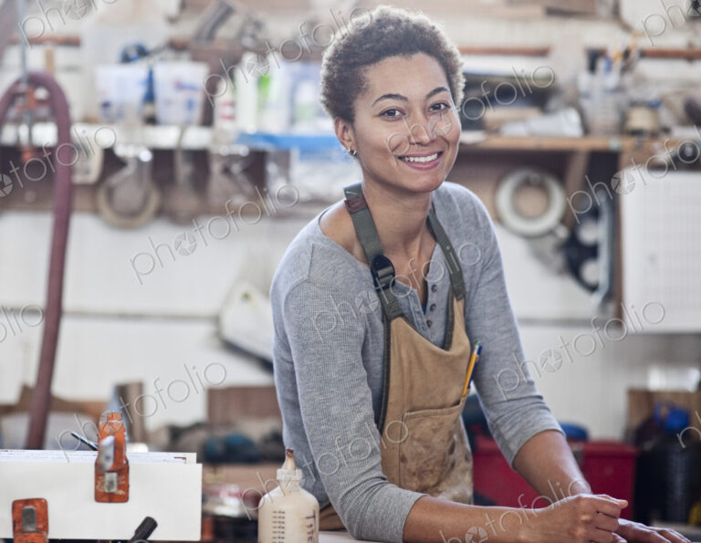 View of a smiling black woman factory worker at her work station in a woodworking factory.