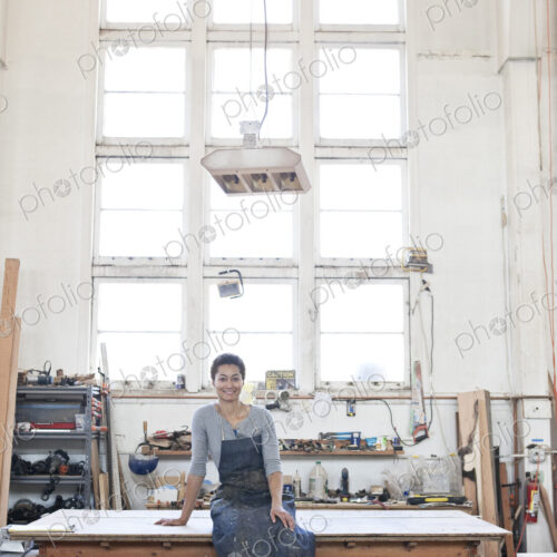 View of a smiling black woman factory worker at her work station in a woodworking factory.