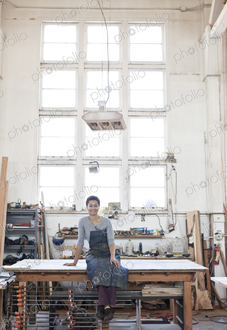 View of a smiling black woman factory worker at her work station in a woodworking factory.