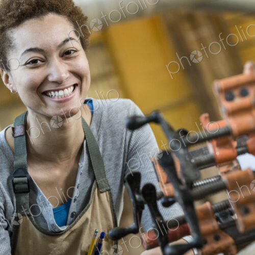 View of a smiling black woman factory worker at her work station in a woodworking factory.
