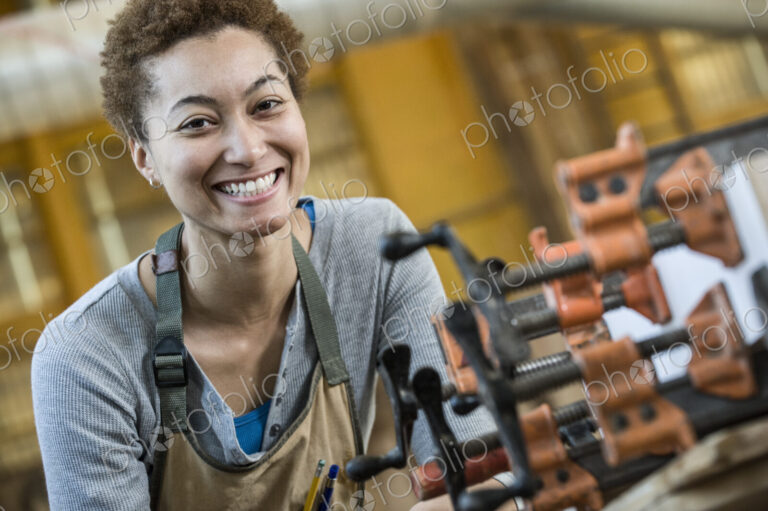 View of a smiling black woman factory worker at her work station in a woodworking factory.