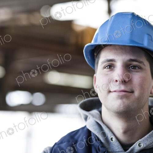 View of a young caucasian factory worker wearing a hard hat in a factory. View of a young caucasian factory worker wearing a hard hat in a factory.