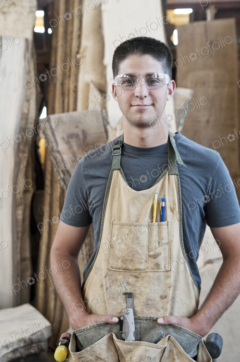 View of a young caucasian man factory worker wearing an apron in a woodworking factory.